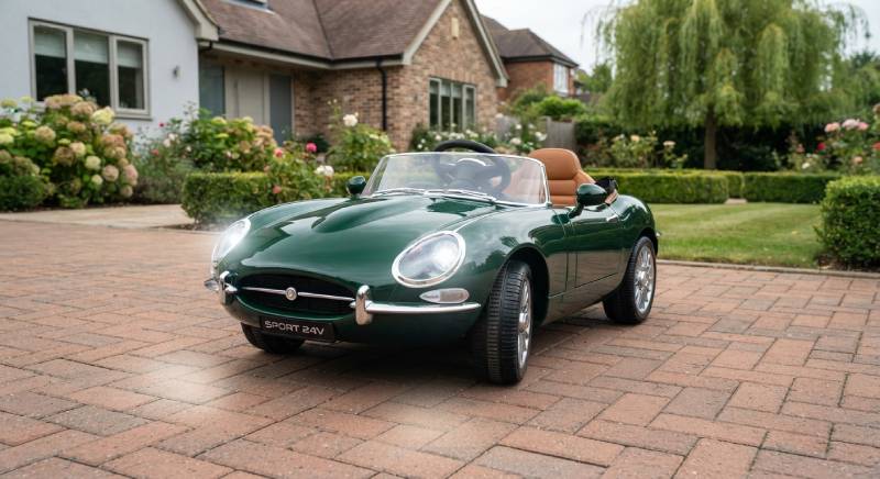 Premium British racing green kids electric car with realistic LED headlights on a suburban driveway